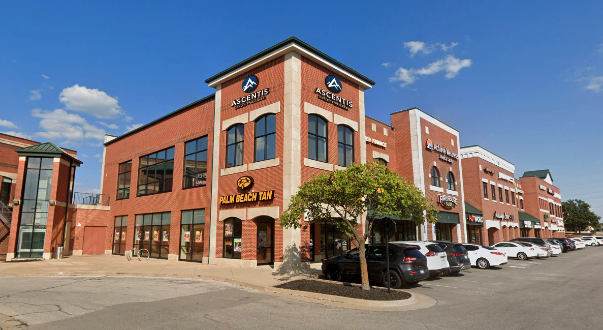 Red brick two-story building for Ascentis Health & Wellness surrounded by other businesses and parked cars
