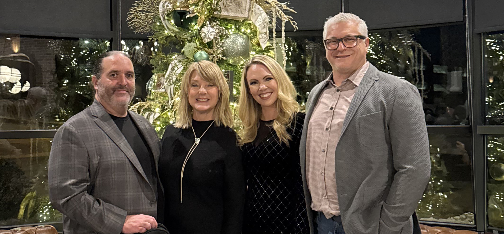 Group photo of two men and two women, smiling for a holiday photo with a Christmas tree